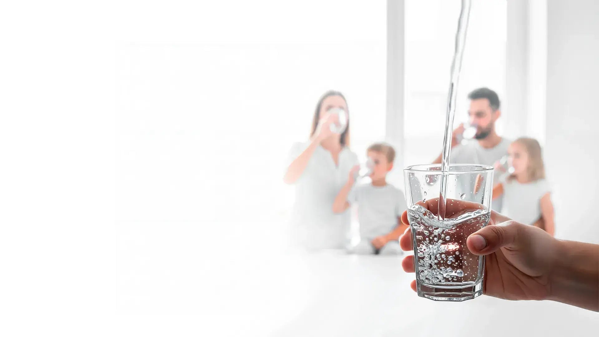 A hand holding a glass of fresh filtered water with a happy family in the background.